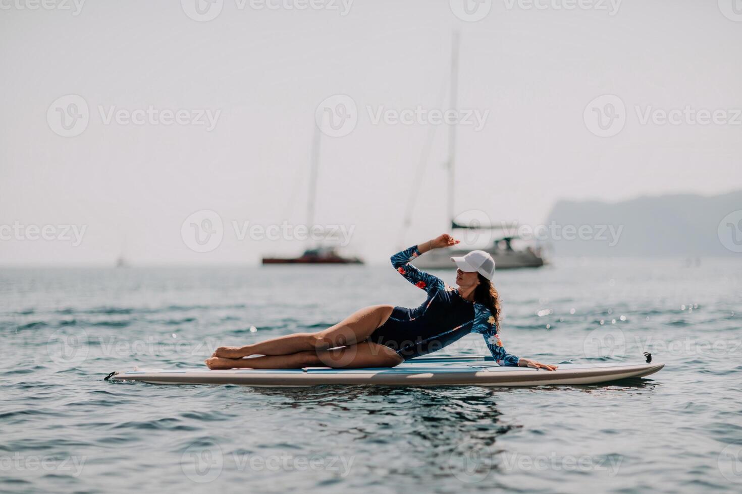 Woman sup yoga. Middle age sporty woman practising yoga pilates on paddle sup surfboard. Female stretching doing workout on sea water. Modern individual female hipster outdoor summer sport activity. photo