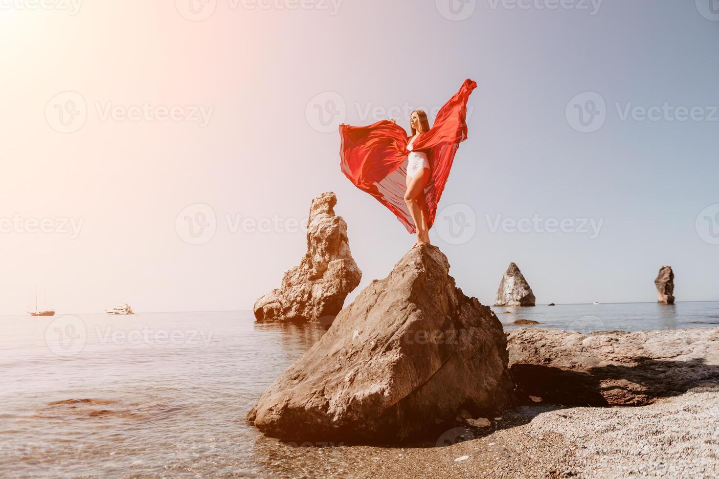 Woman travel sea. Young Happy woman in a long red dress posing on a beach near the sea on background of volcanic rocks, like in Iceland, sharing travel adventure journey photo