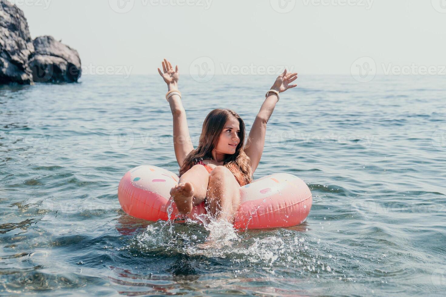mujer verano mar. contento mujer nadando con inflable rosquilla en el playa en verano soleado día, rodeado por volcánico montañas. verano vacaciones concepto. foto