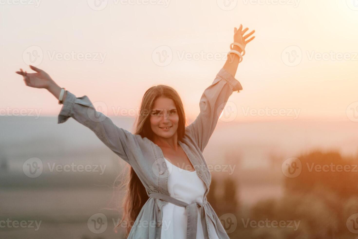 Happy woman standing with her back on the sunset in nature in summer with open hands. Romantic beautiful bride in white boho dress posing with mountains on sunset photo