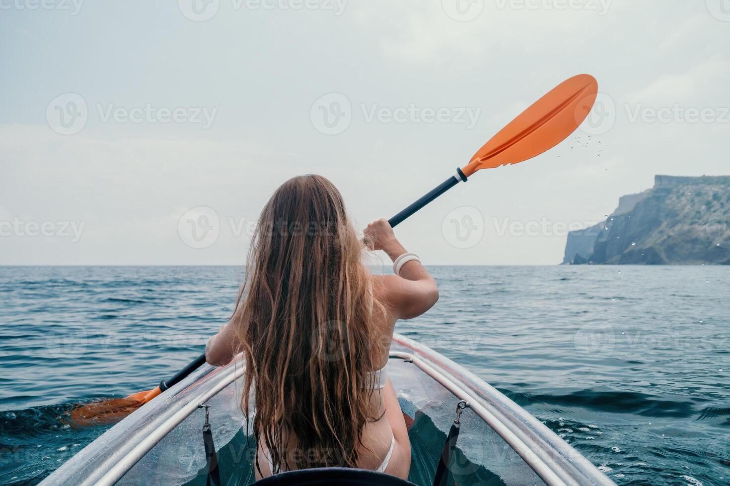 Woman in kayak back view. Happy young woman with long hair floating in transparent kayak on the crystal clear sea. Summer holiday vacation and cheerful female people relaxing having fun on the boat photo