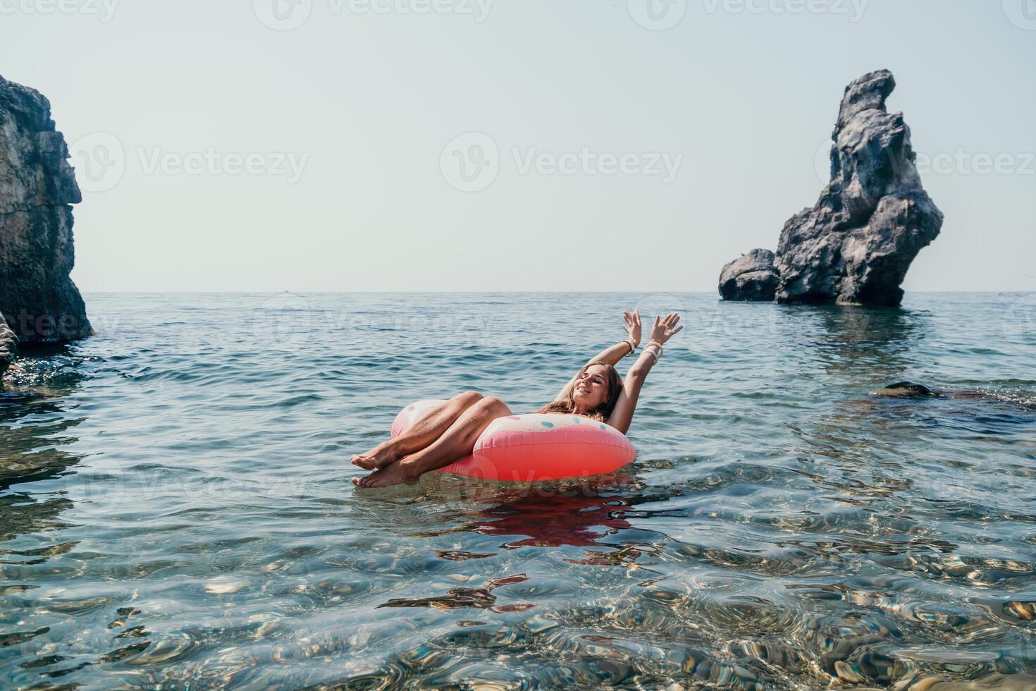 mujer verano mar. contento mujer nadando con inflable rosquilla en el playa en verano soleado día, rodeado por volcánico montañas. verano vacaciones concepto. foto