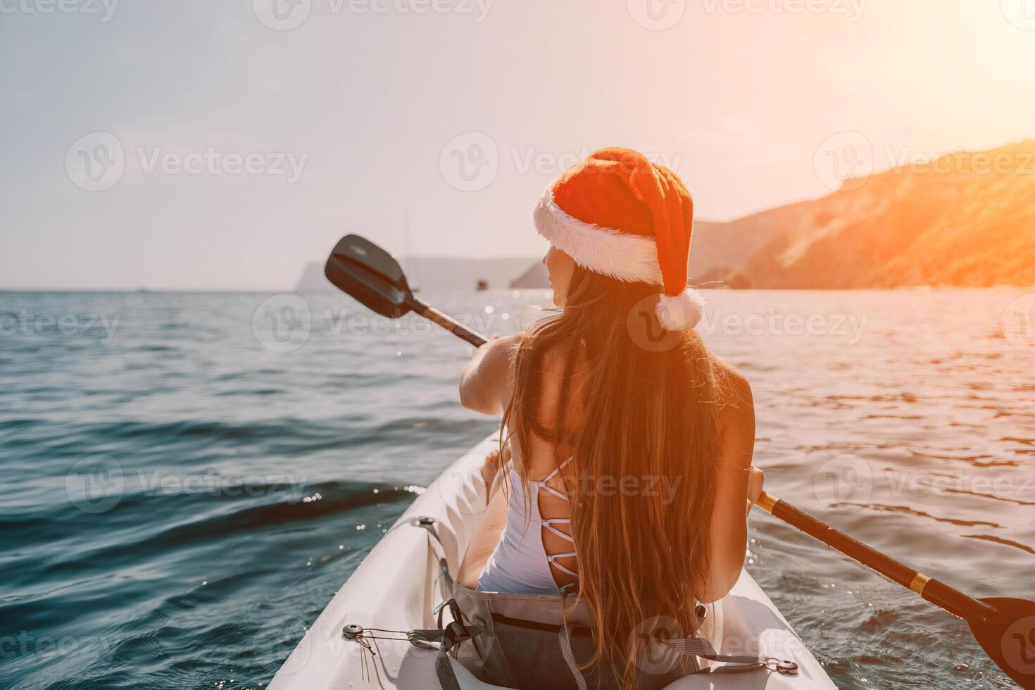 Woman in kayak back view. Happy young woman in Santa hat floating in kayak on calm sea. Summer holiday vacation and cheerful female people relaxing having fun on the boat. photo