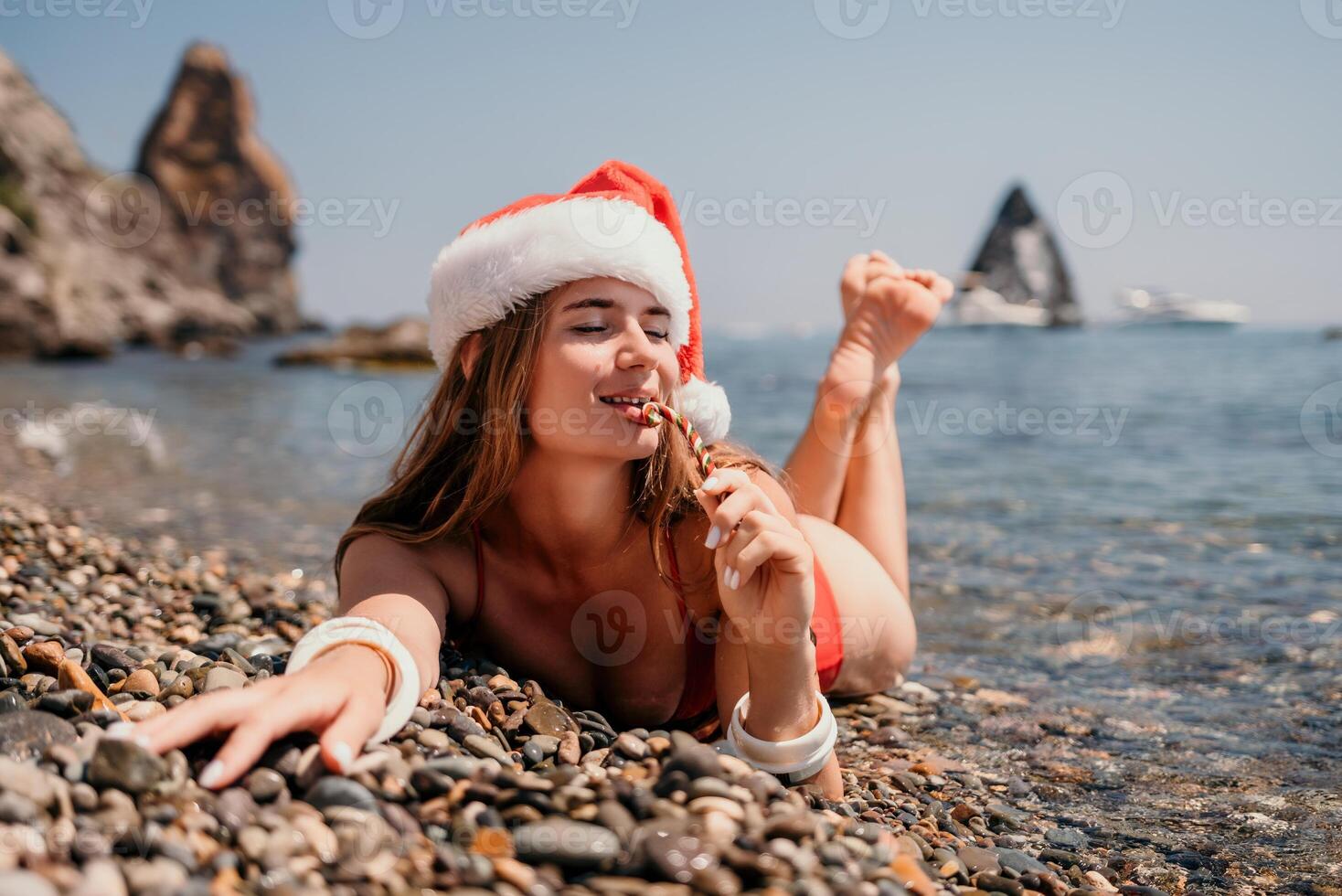 Woman travel sea. Happy tourist enjoy taking picture on the beach for memories. Woman traveler in Santa hat looks at camera on the sea bay, sharing travel adventure journey photo