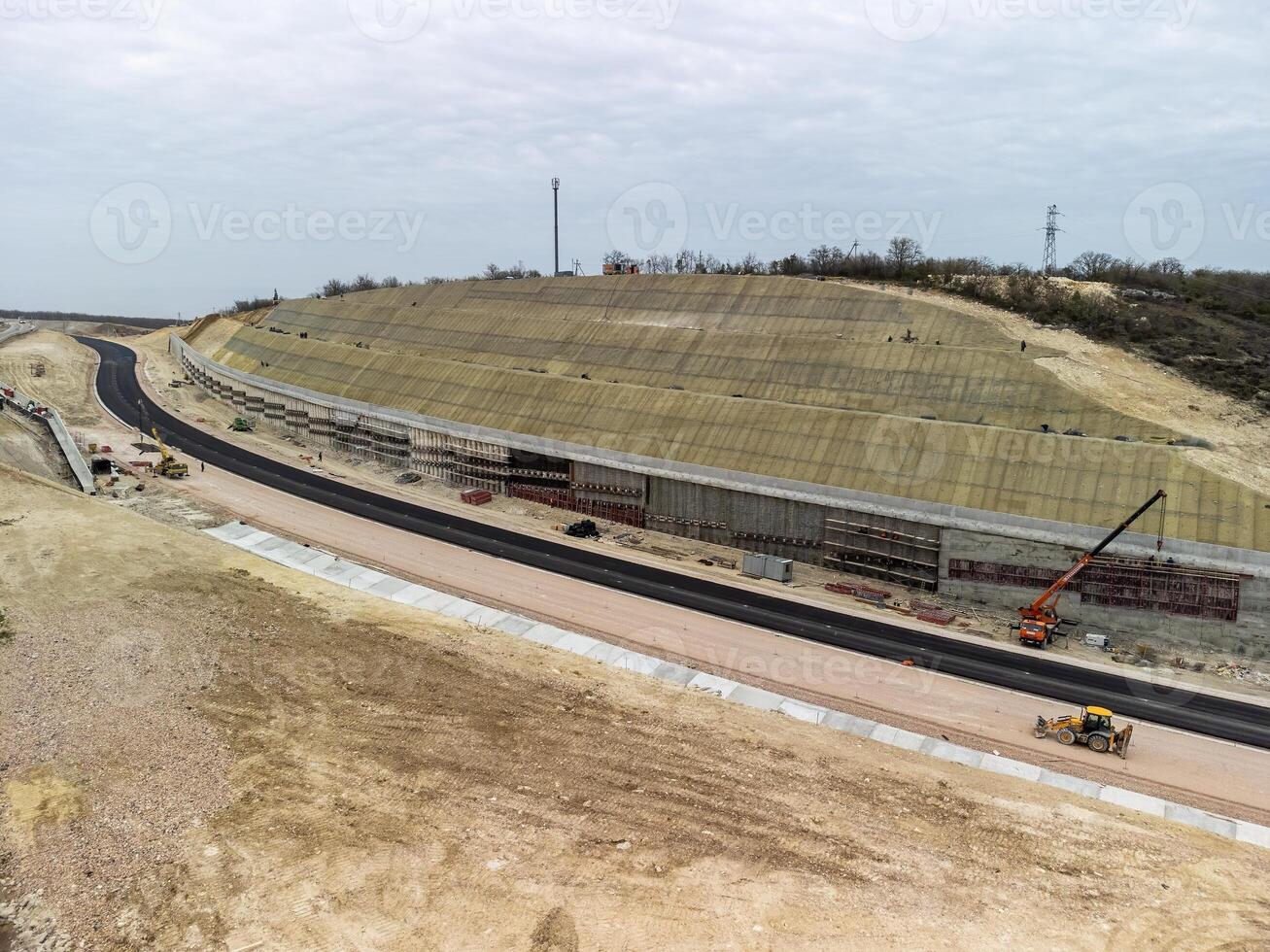 Mountain road constraction. Workers reinforce the slope over the new road. Road construction in progress on slope nature canyon. Infrastructure development and logistics. Aerial drone shot photo