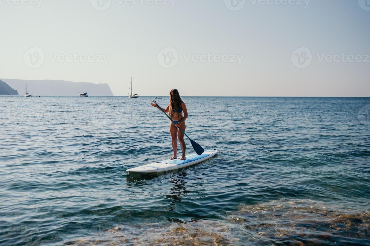 Woman sea sup. Close up portrait of happy young caucasian woman with long hair looking at camera and smiling. Cute woman portrait in a blue bikini posing on sup board in the sea photo