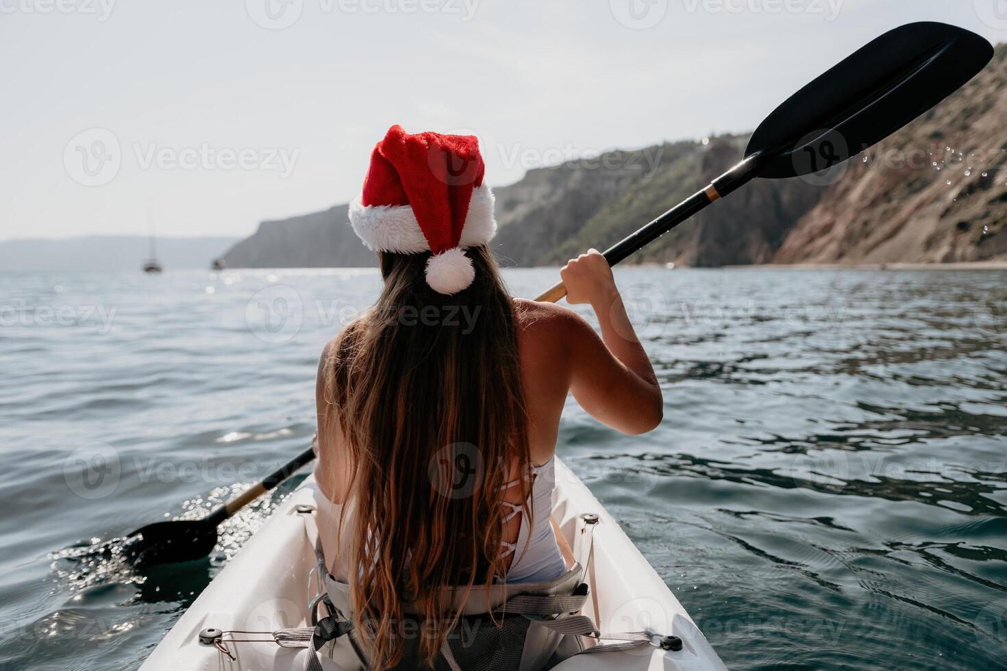 Woman in kayak back view. Happy young woman in Santa hat floating in kayak on calm sea. Summer holiday vacation and cheerful female people relaxing having fun on the boat. photo