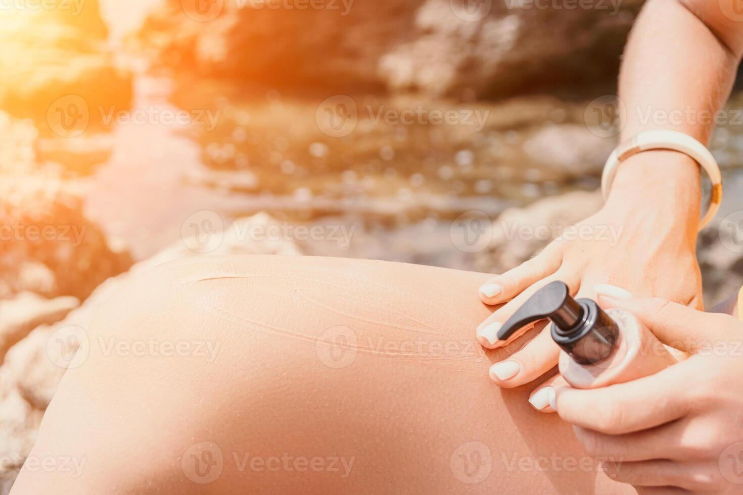 Suntan Lotion. Sexy Woman in bikini apply sun protection cream on her smooth tanned legs. Skin care. Legs on the beach. Close up of female legs with smearing moisturizing lotion. Sunblock concept. photo