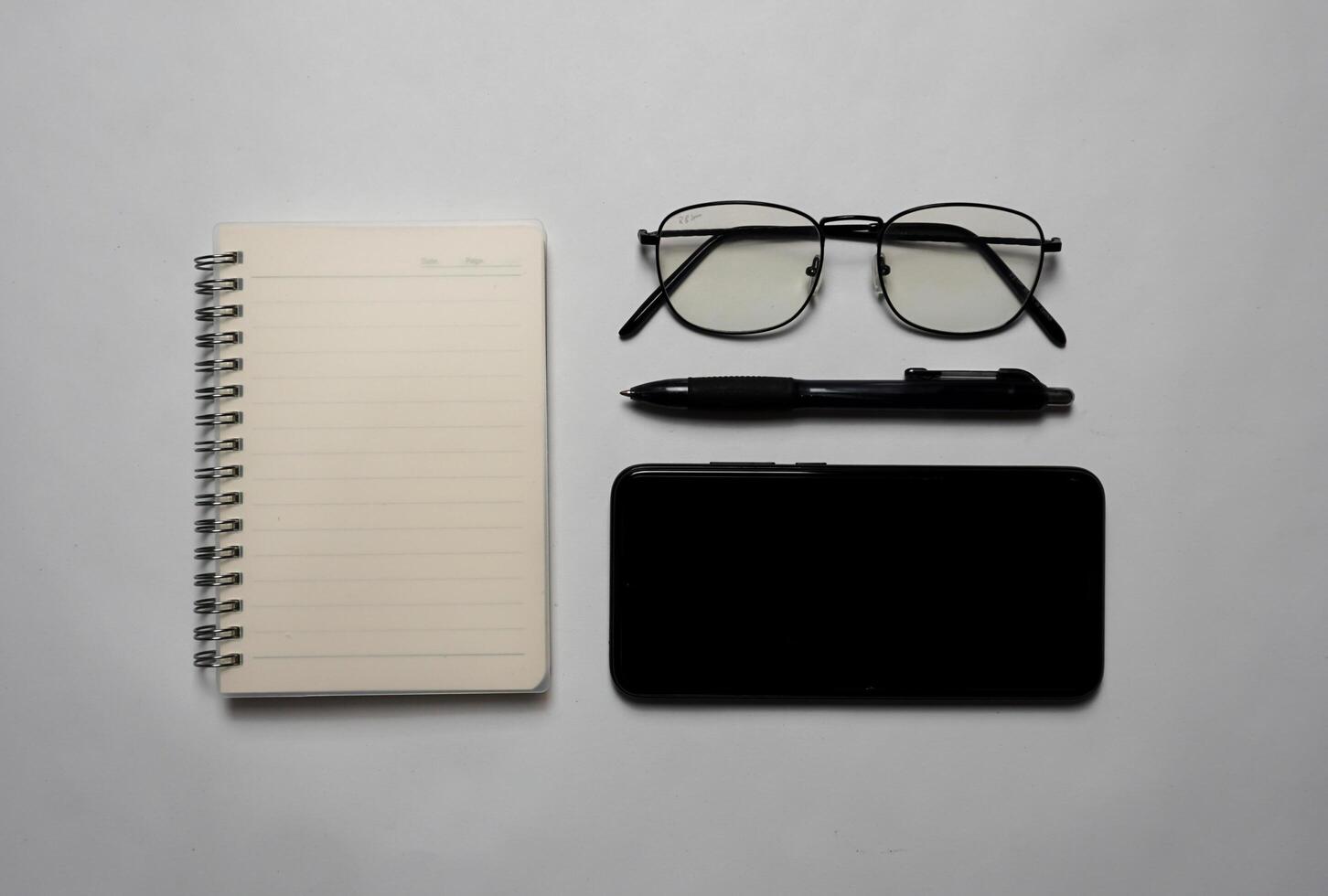 Seen from above there is a notebook with a pen, glasses and a smartphone. photo