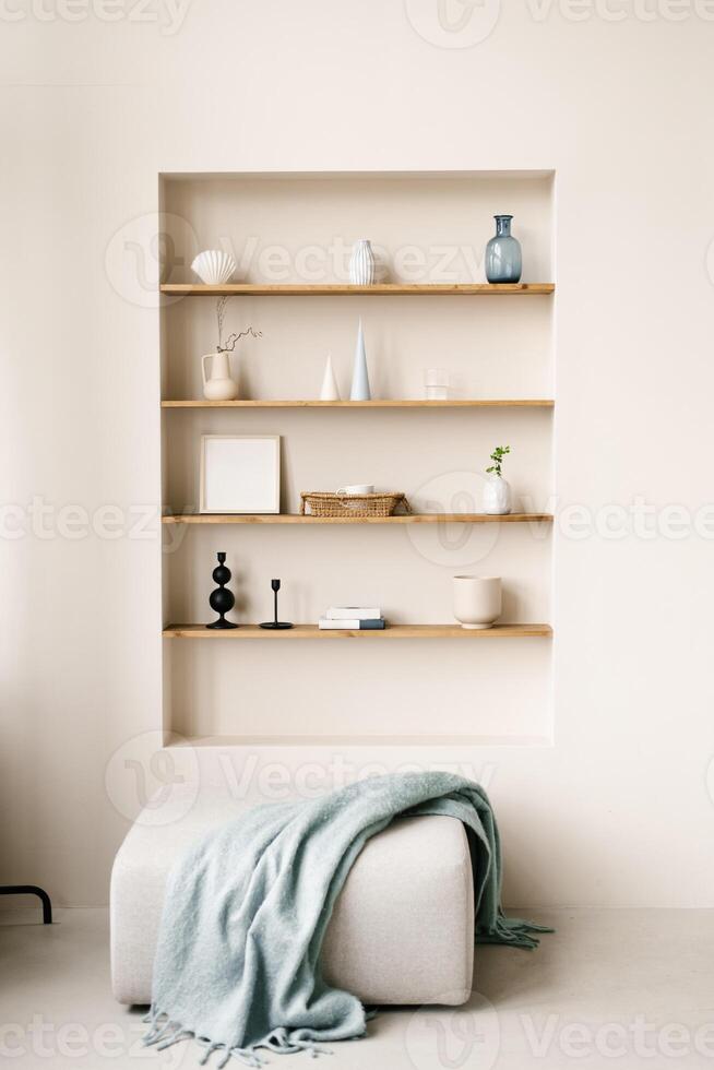 Modern living room with pouf with blue blanket. Built-in shelves in the wall with decor, personal accessories, ceramics in Scandinavian minimalist style photo