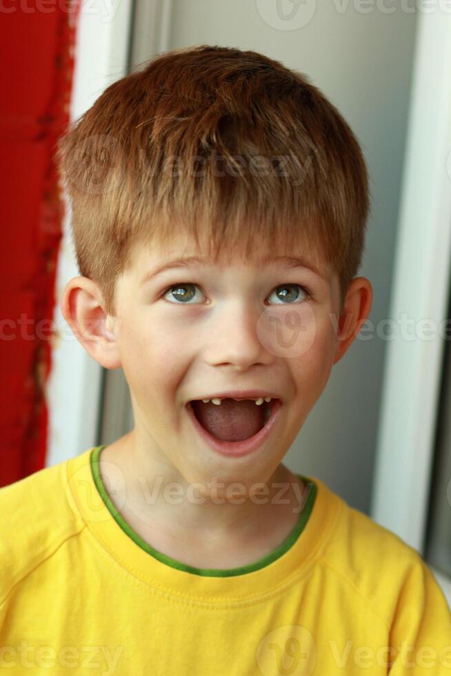 Close up portrait of a boy in a yellow T-shirt with his mouth wide open whose front top milk teeth have fallen out photo