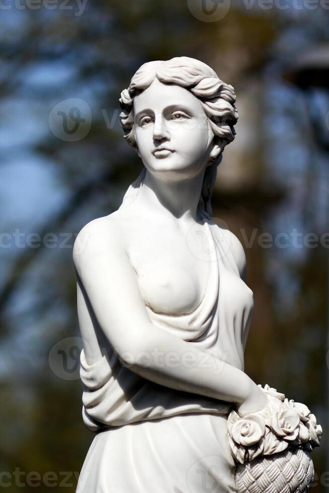 Classic white marble statue of Demeter, the goddess of harvest, young lady holding a basket of roses photo