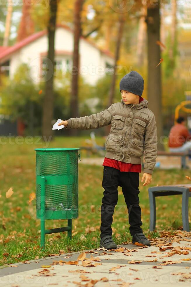 Full length portrait of a six year old boy throwing paper to the trash bin garbage can in the autumn park photo