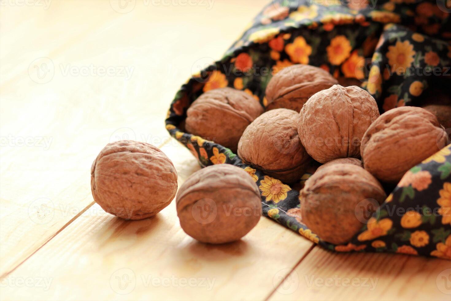 Walnuts scattered from floral pattern bag on sunlit light brown wooden floor photo