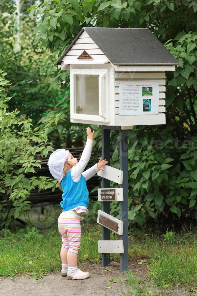 Little girl trying to get a book out of a community public street library. Book crossing. photo