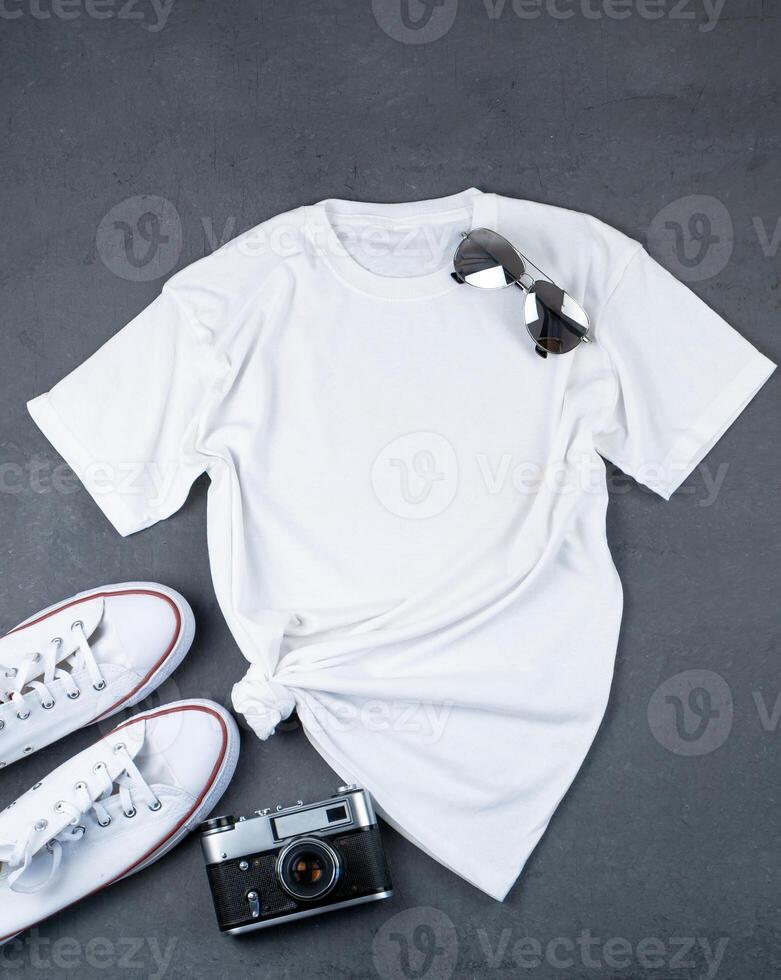 blanco camiseta con sitio para texto. zapatillas, anteojos, cámara - un conjunto de ropa para caminando. camiseta Bosquejo para impresión. elegante equipo. gris antecedentes con Copiar espacio foto