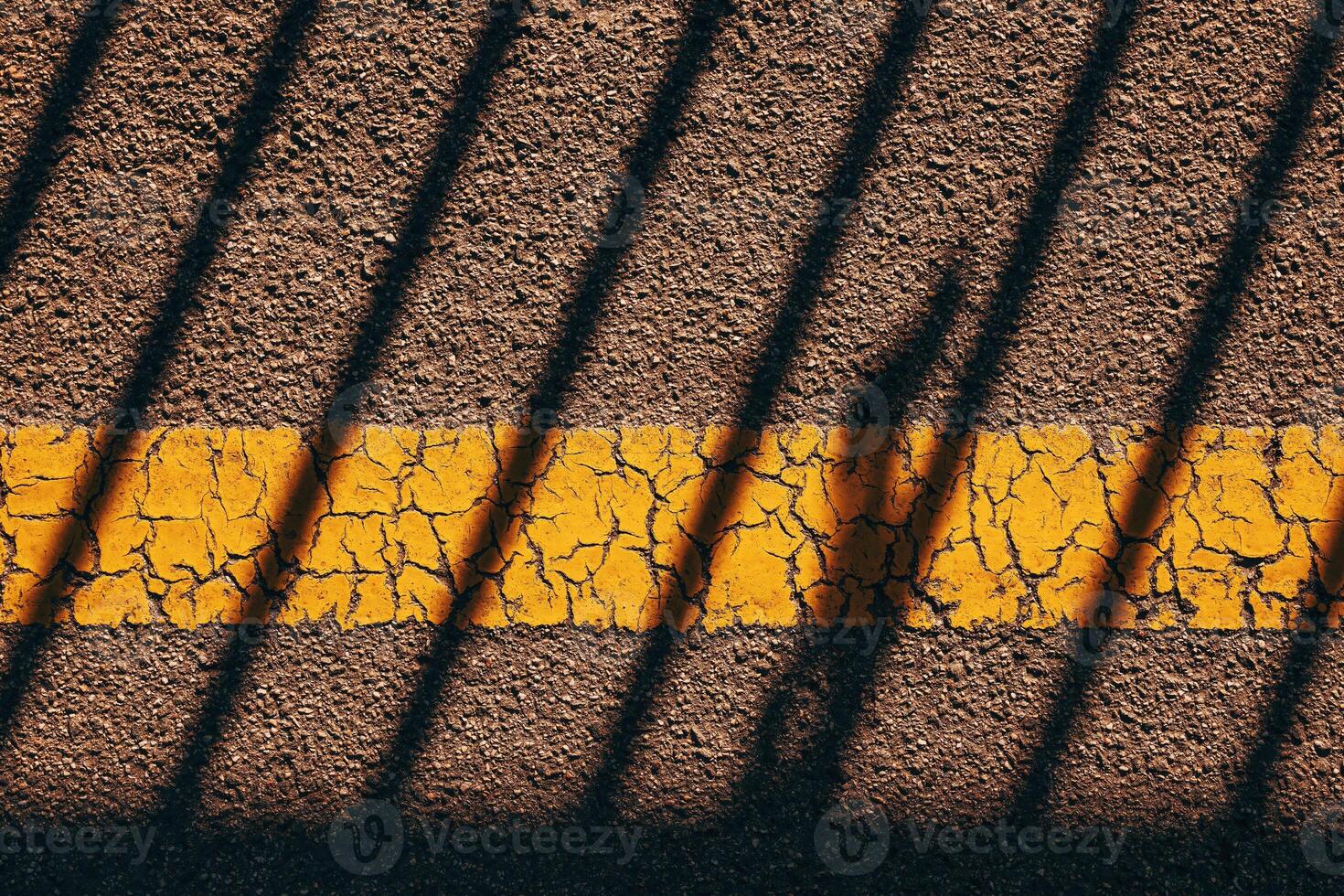 Asphalt sidewalk surface with worn yellow line and striped shadow striped pattern as background photo