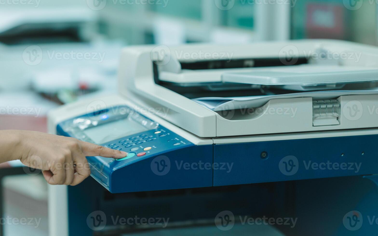 A employee is pointing at a printer, which is on and ready to print. The staff is likely preparing to print something, such as a document or a photo