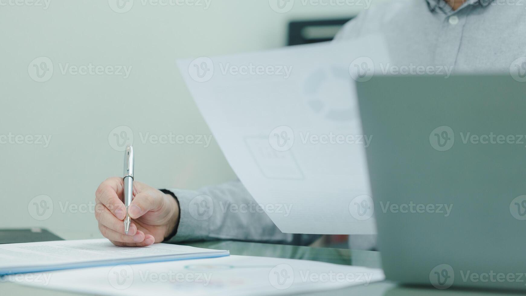 Businessman is writing with a pen on a piece of paper. Paper is on a desk next to a laptop. businessperson is focused on his writing, and the scene suggests a sense of concentration and productivity photo