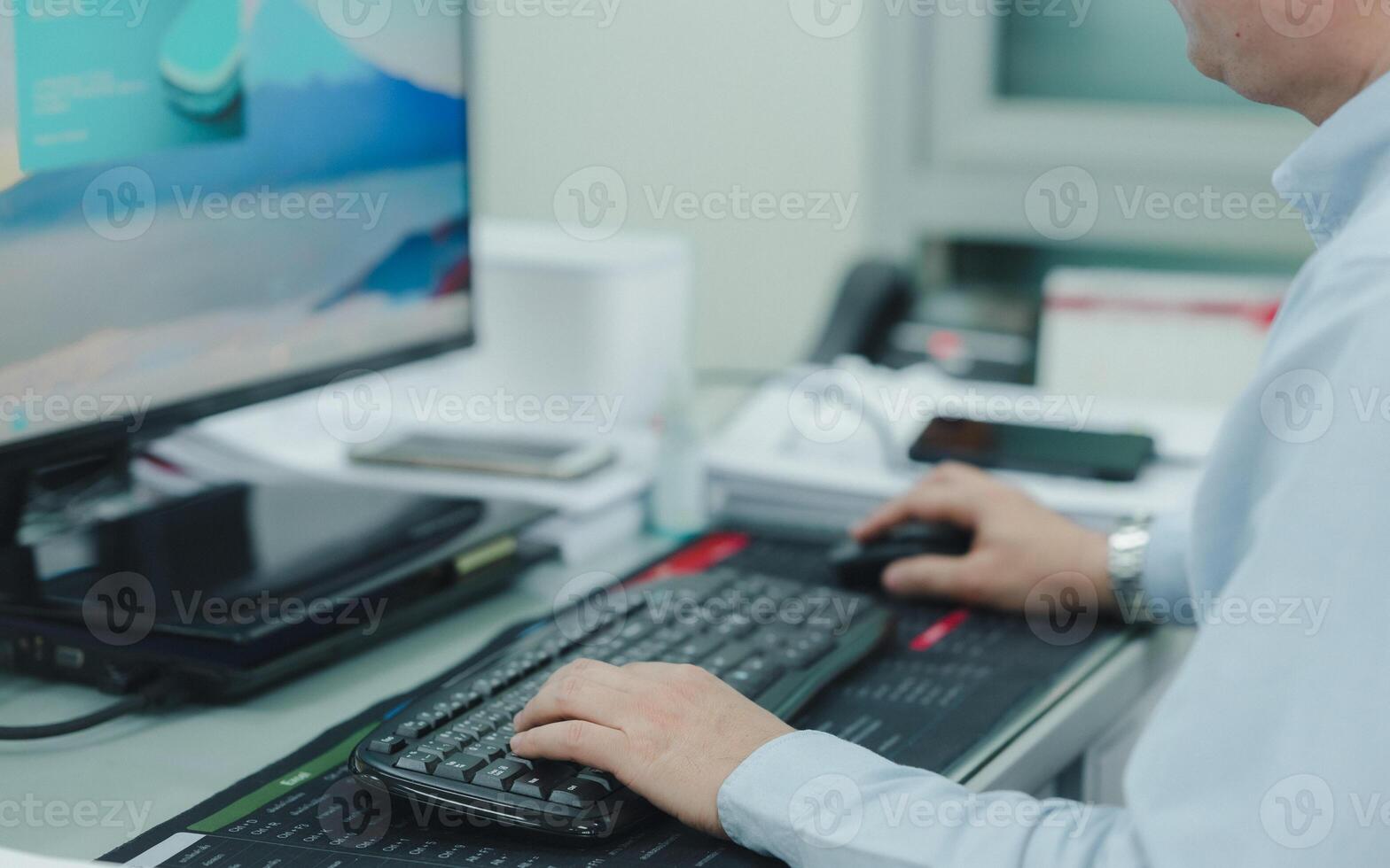 un ingeniero o programador es mecanografía en un computadora teclado en frente de un monitor. él es vistiendo un azul camisa y un mirar, trabajo colaborativo foto