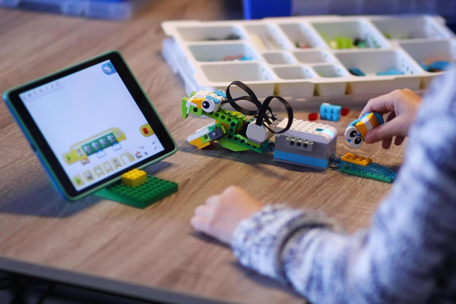 Kyiv, Ukraine - December 1, 2018 Closeup of boy's hands constructing lego robot and programming it at robotics lesson at school photo