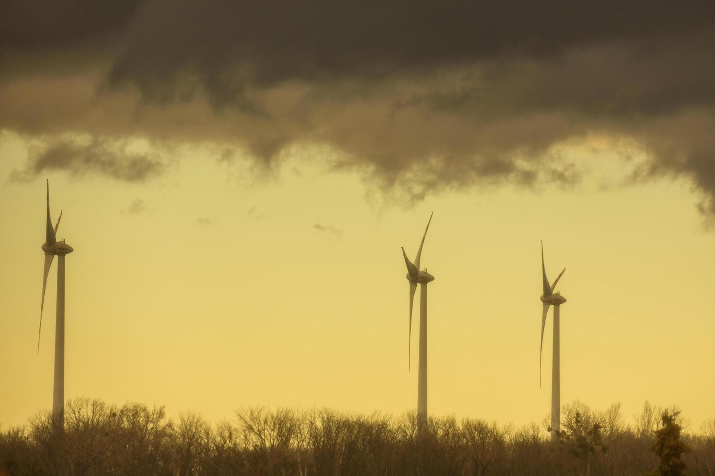 Tres molinos de viento en un plano paisaje con oscuro nubes de lluvia y amarillo color foto