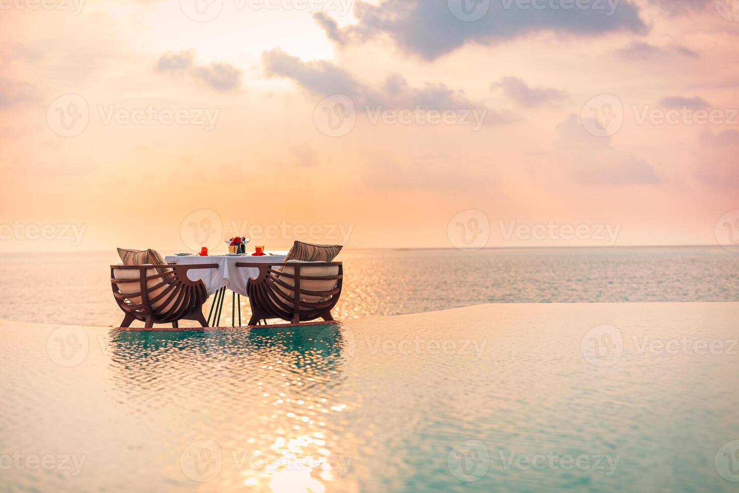 Seascape view under sunset light with dining table with infinity pool around. Romantic tropical getaway for two, couple concept. Chairs, food and romance. Luxury destination dining, honeymoon template photo