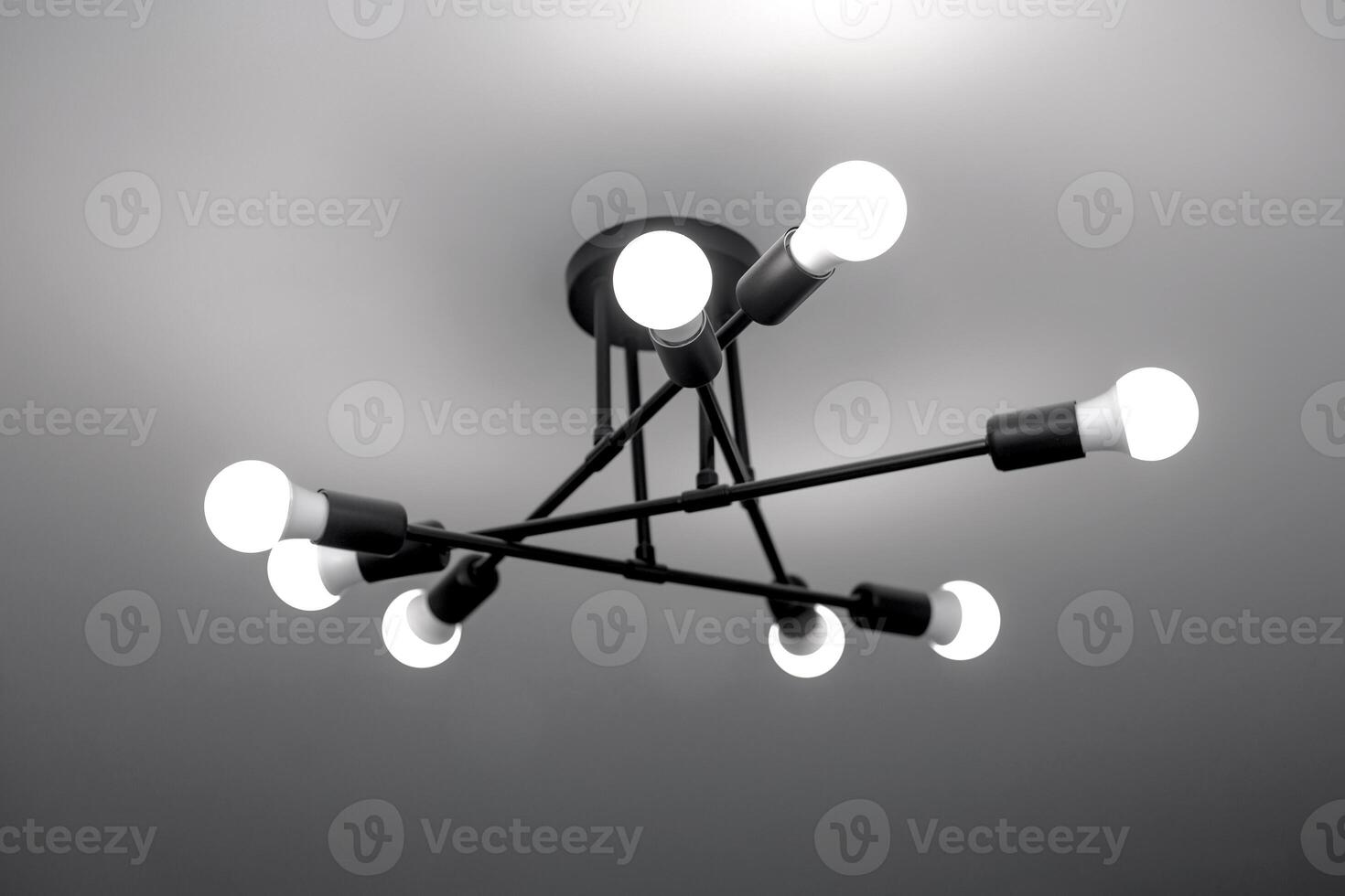 black chandelier in loft style on a white stretch ceiling with white light photo