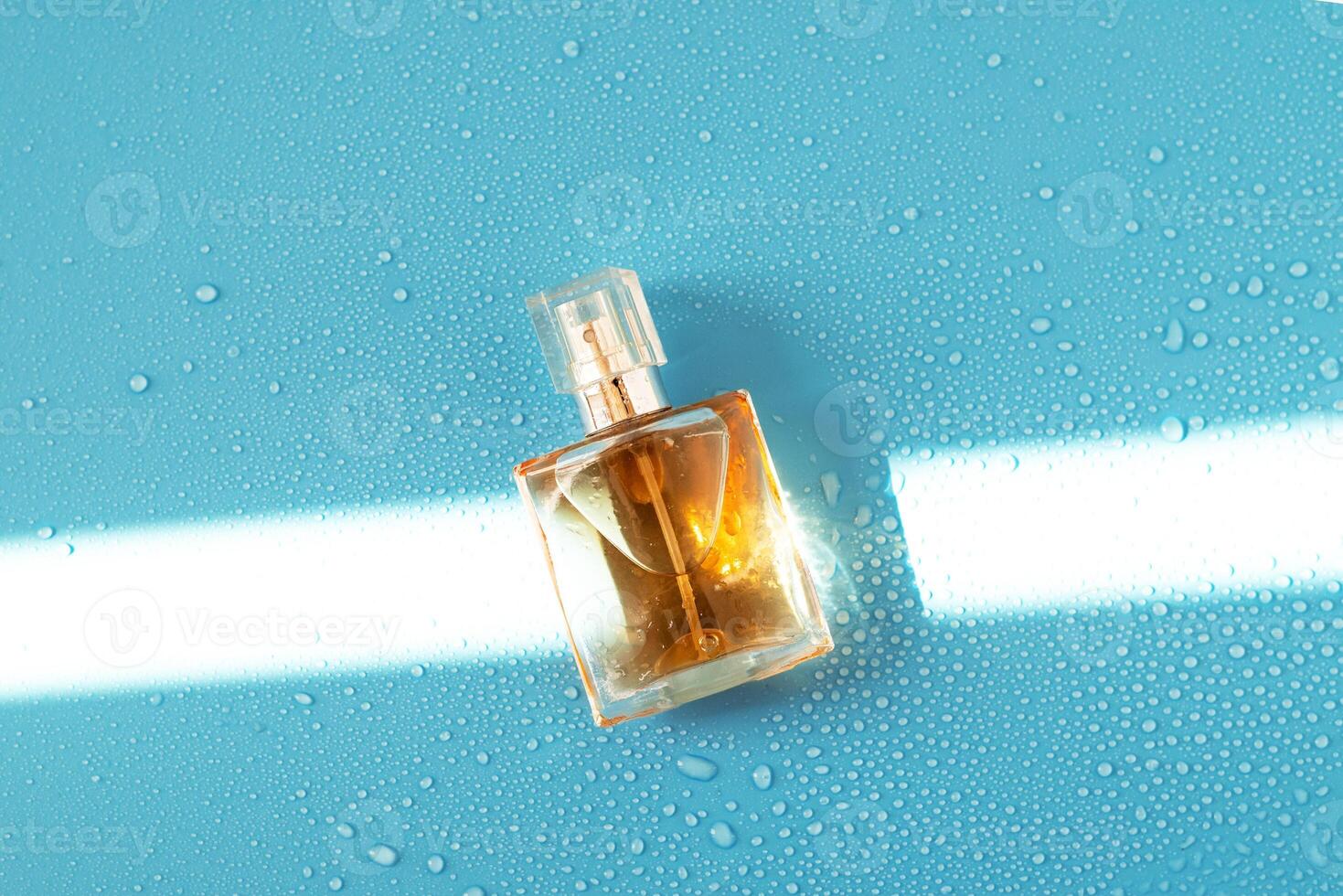 Perfume woman bottle on blue background with hard light and water drops. with shadows flat lay, top view photo