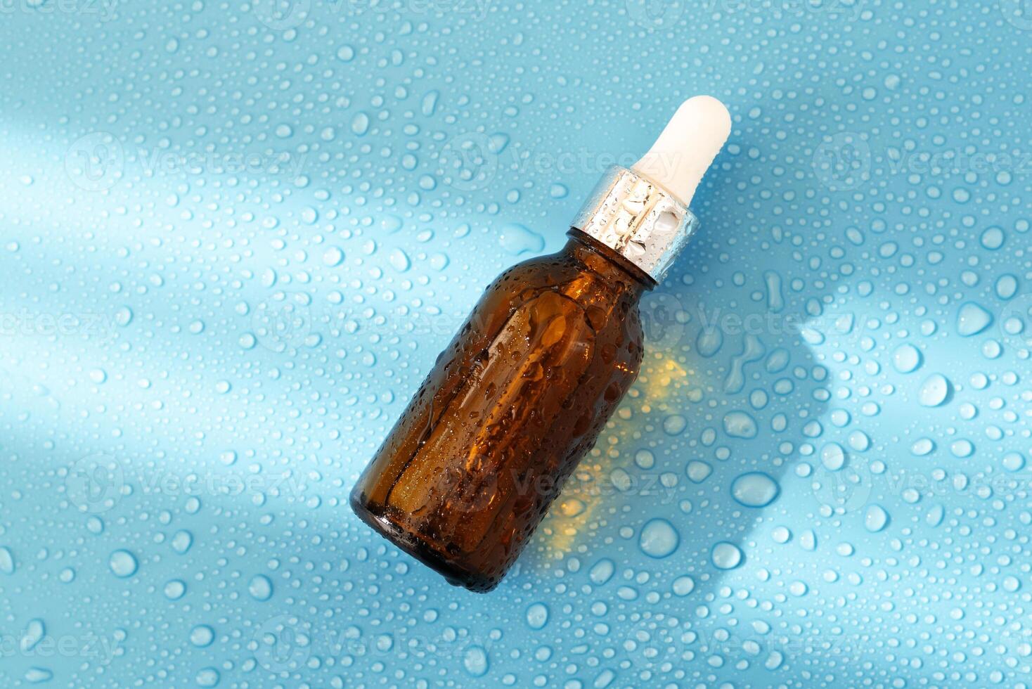 Serum bottle , oil cosmetic on blue background with hard light and water drops. with shadows flat lay, top view photo
