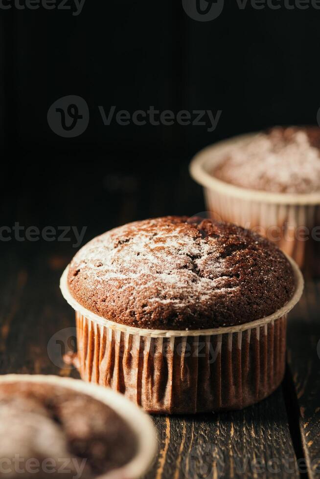 Chocolate muffins with powdered sugar on a black background. Still life close up. Dark moody. Food photo. photo