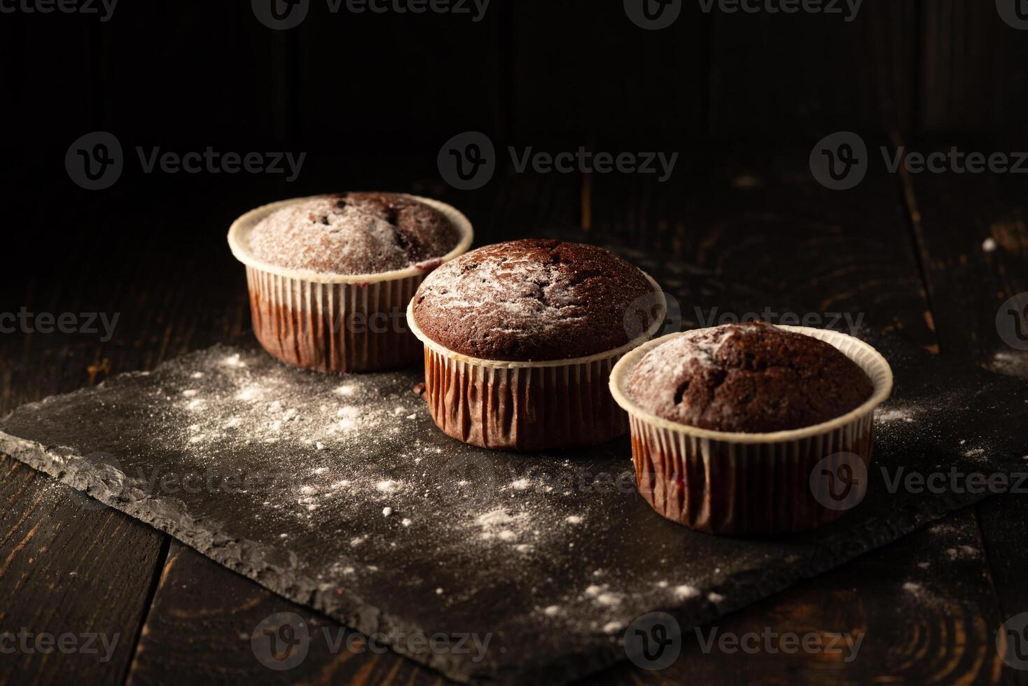 Chocolate muffins with powdered sugar on a black background. Still life close up. Dark moody. Food photo. photo