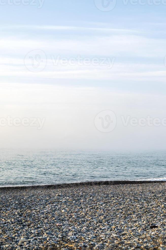 Seascape view of nature on the coast of a beach and ocean water on a Summer day. Beautiful scenery of a sea shore filled with rocky sand textures and the blue sky on the horizon and fog. photo