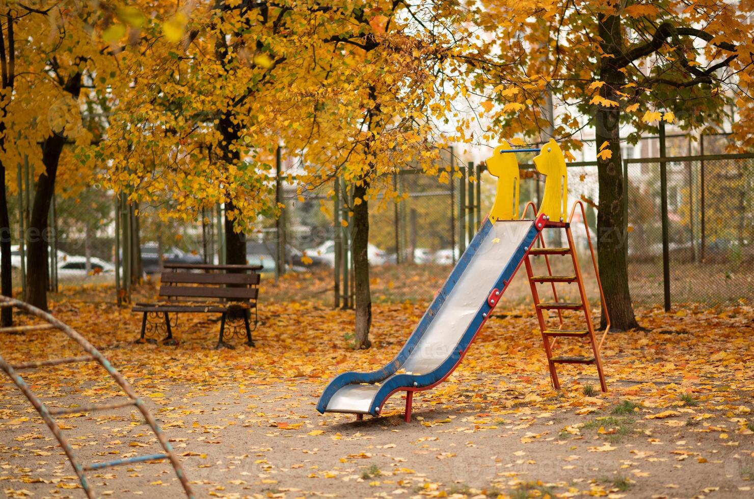 Empty playground with a beautiful orange and red Autumn background. old children slide with maple leaves at autumn photo