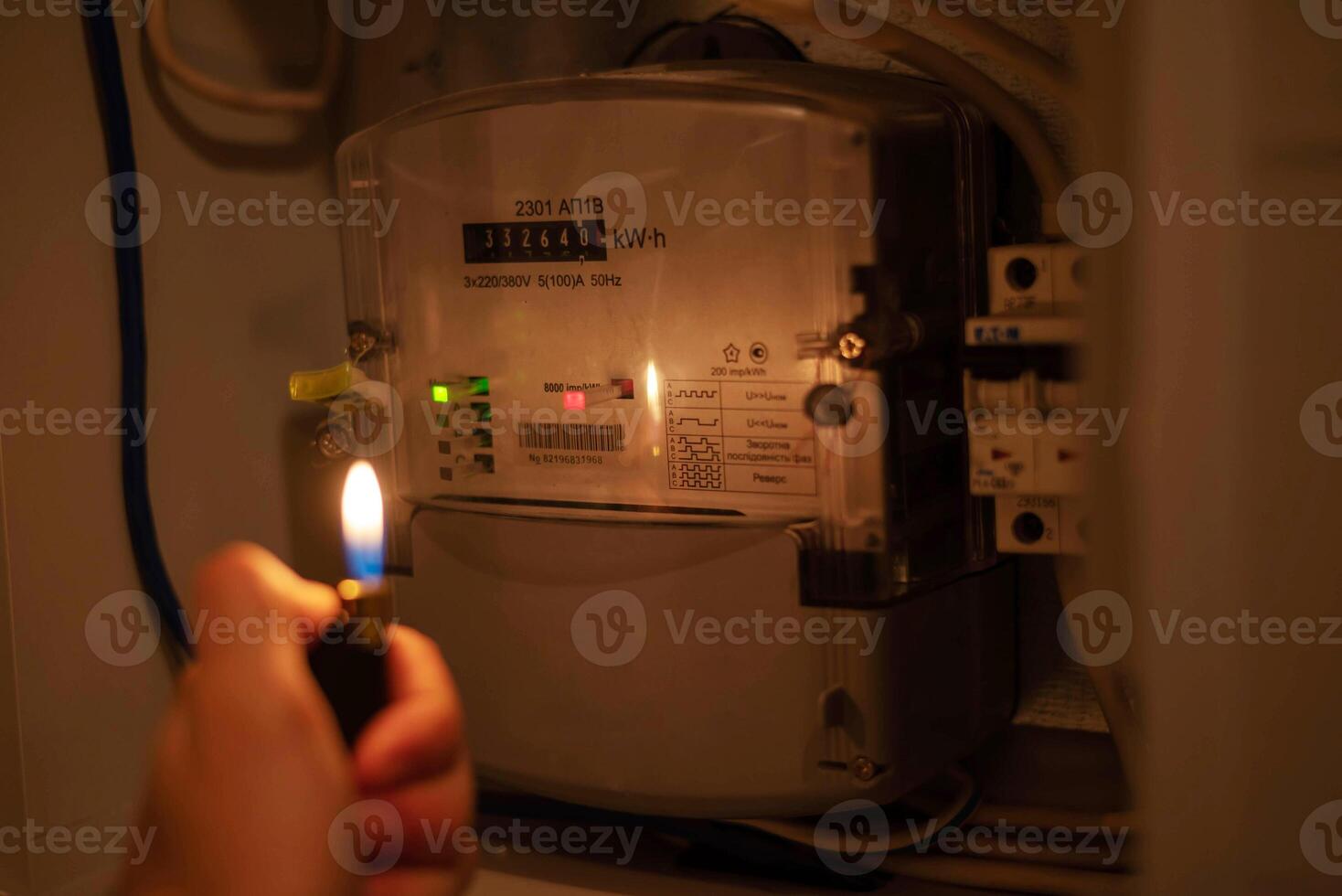 A man's hand with a lighter in complete darkness looks at the electric meter at home. Power outage, blackout concept. photo