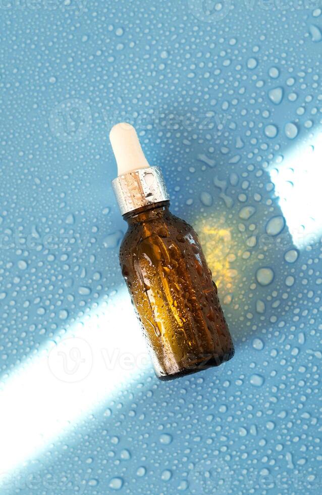 Serum bottle , oil cosmetic on blue background with hard light and water drops. with shadows flat lay, top view photo