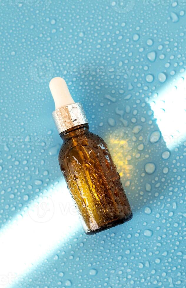 Serum bottle , oil cosmetic on blue background with hard light and water drops. with shadows flat lay, top view photo