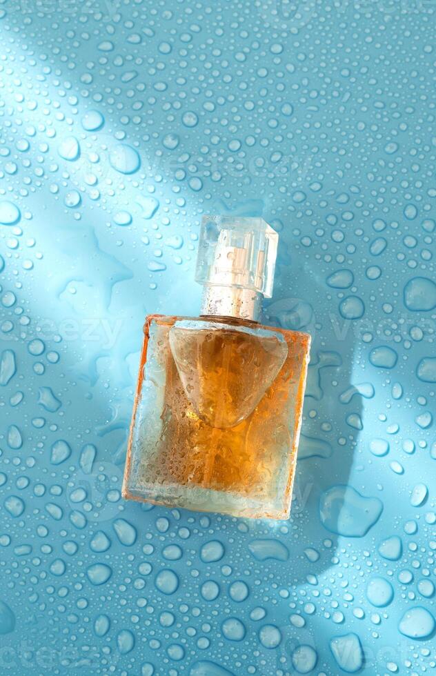 Perfume woman bottle on blue background with hard light and water drops. with shadows flat lay, top view photo