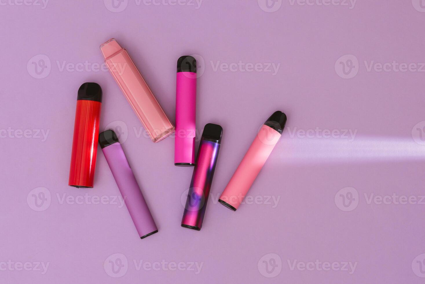 Colorful disposable electronic cigarettes on a purple background. The concept of modern smoking, vaping and nicotine. Top view photo