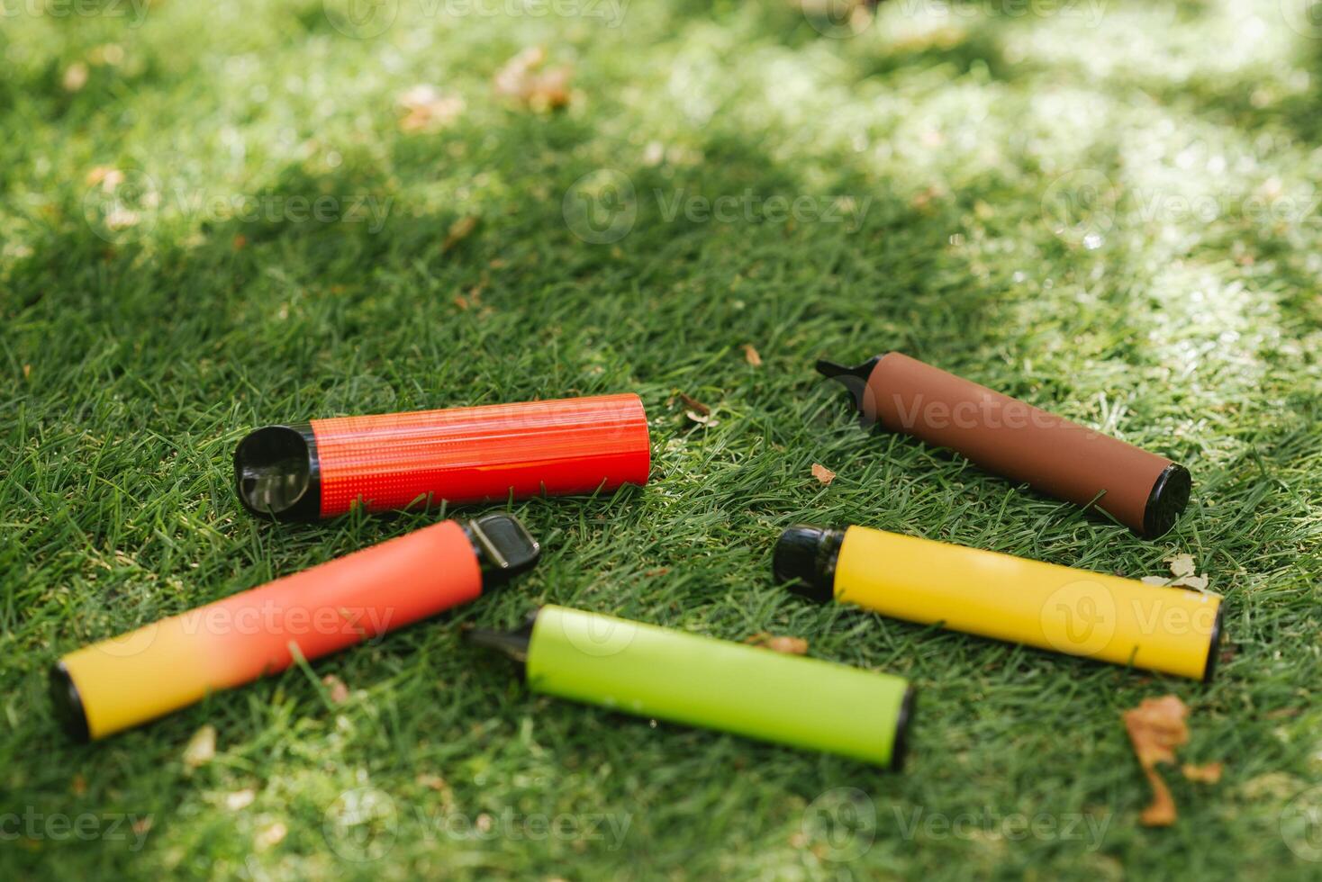 Vaping devices. Set of colorful electronic cigarettes. Electronic sticks for vaping on green grass with sun rays photo