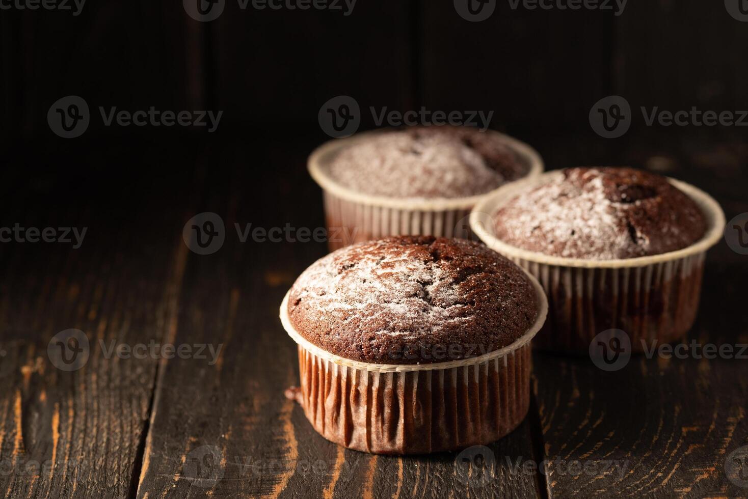 Chocolate muffins with powdered sugar on a black background. Still life close up. Dark moody. Food photo. photo