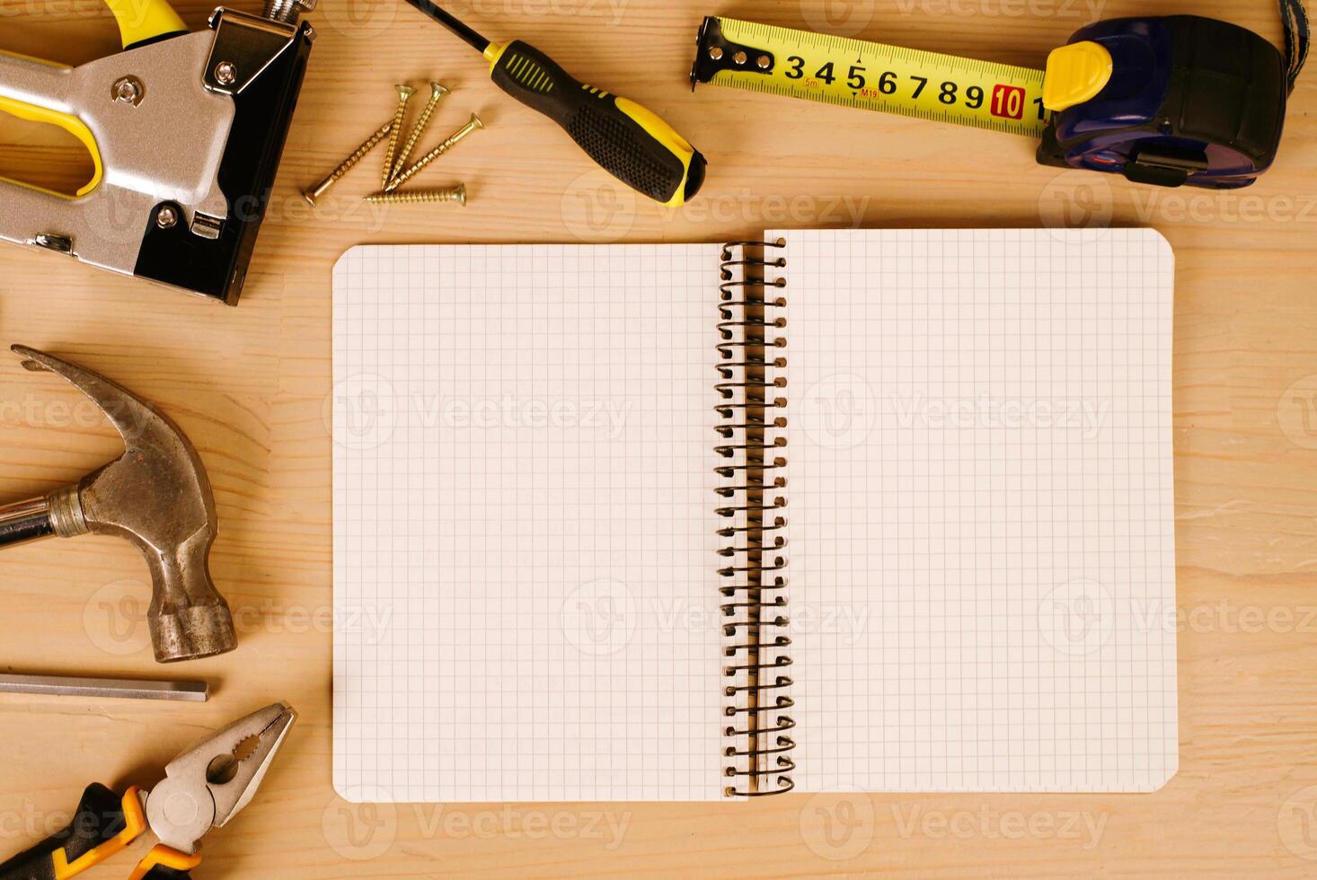 Notepad surrounded by dusty tools on an old wooden background. View from above. workplace pliers, tape measure, screwdriver, hammer and construction stapler photo