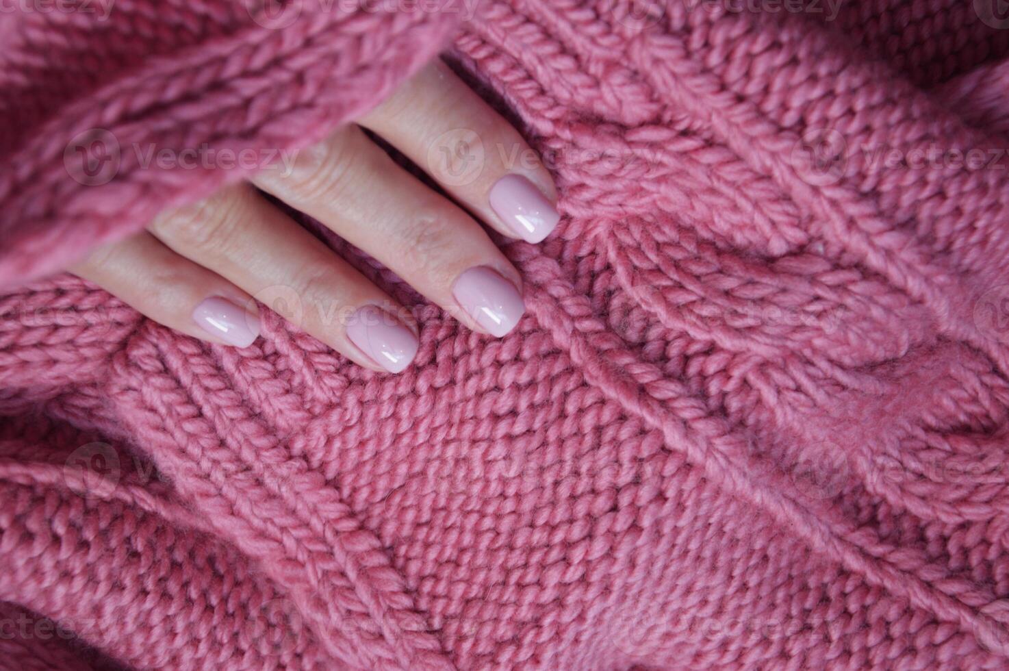 Pink knitted wool scarf, sweater and female hands with professional manicure. Winter hand care. photo