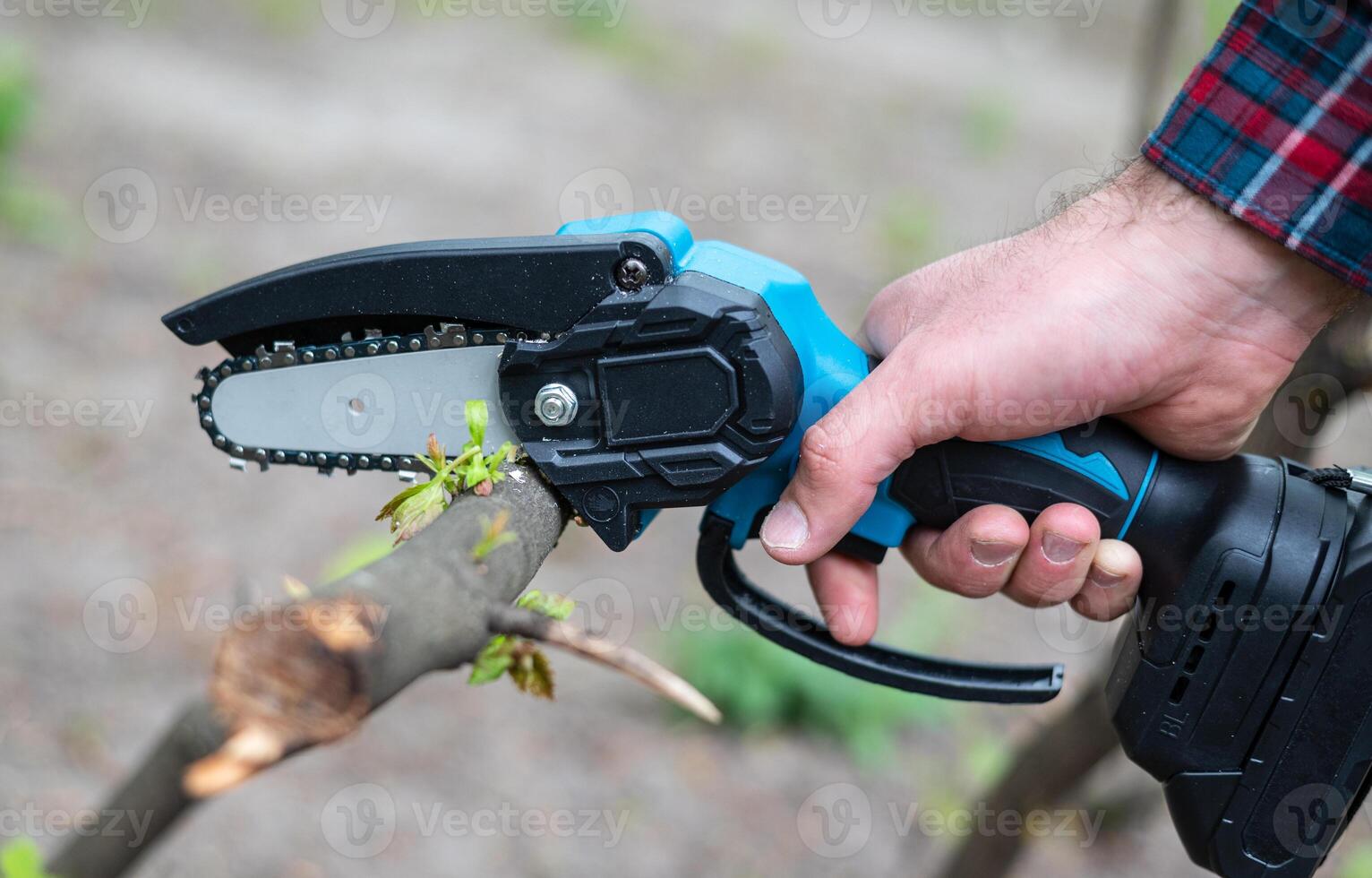 Hand holds light chain saw with battery to trim broken branch of an tree, in sunny day photo