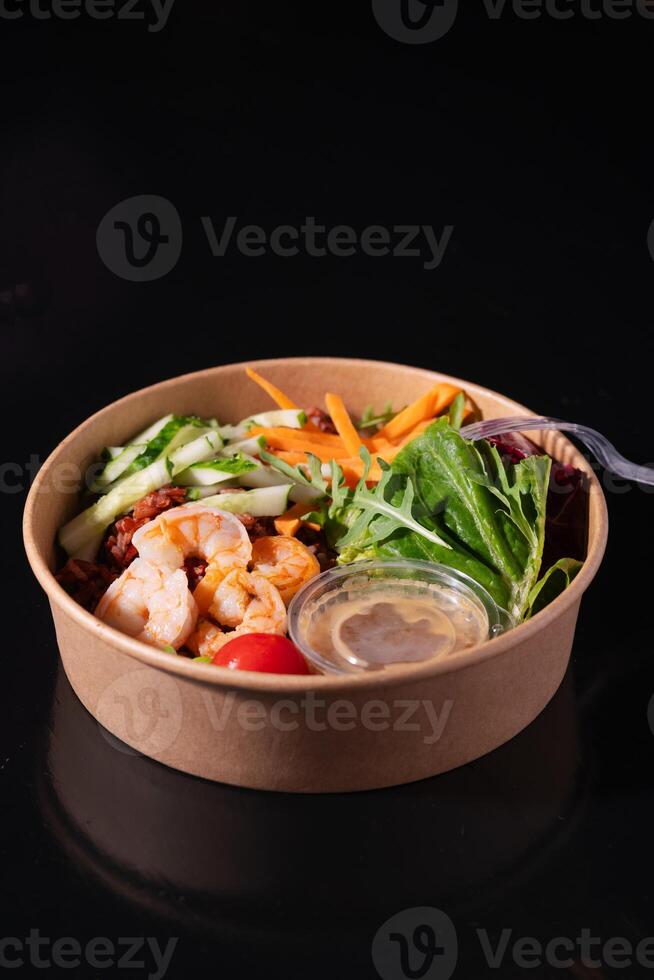 Bowl with shrimps, carrots, cucumbers, beans and vegetables with herbs, on a black background. Healthy food concept photo