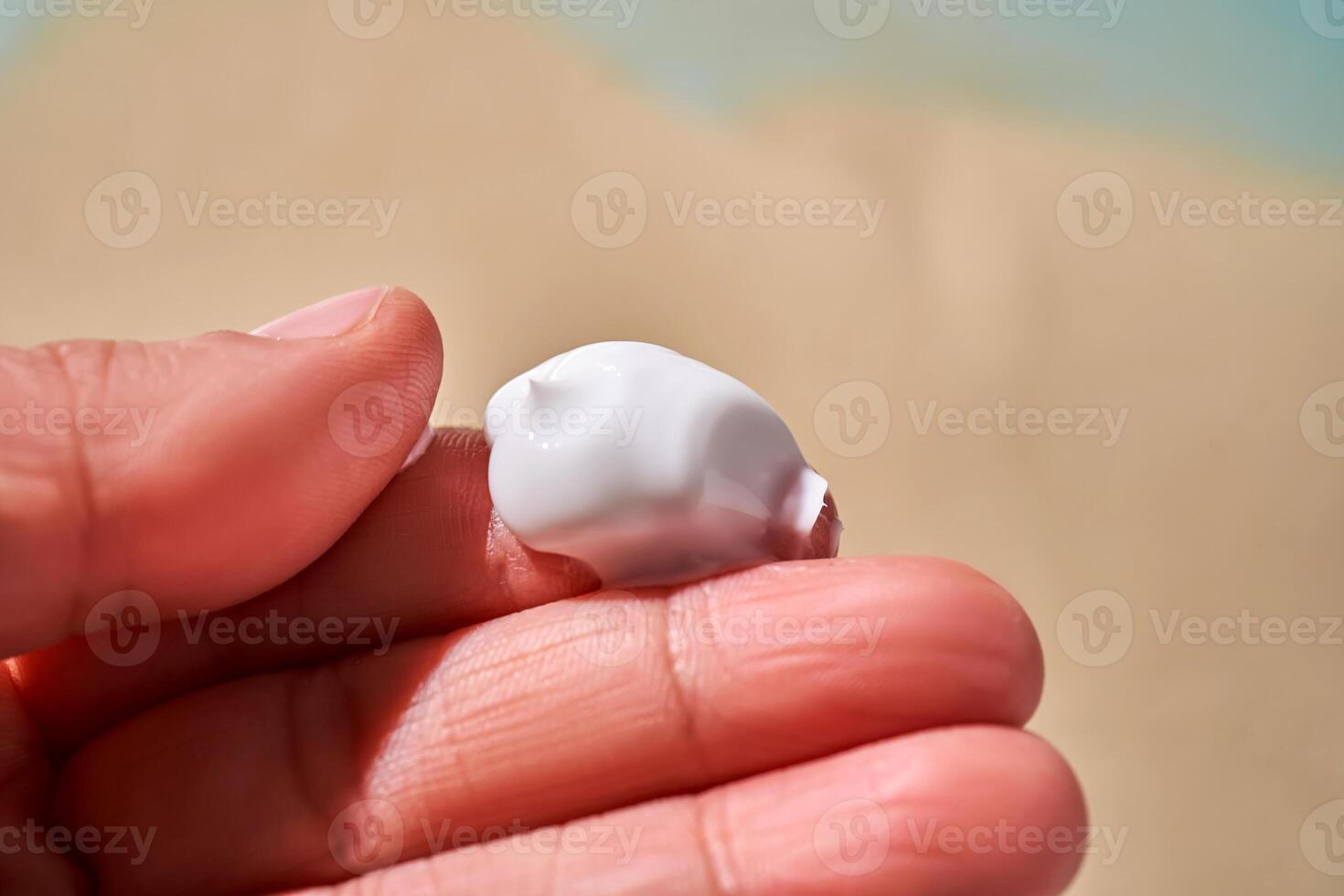 A smear of white cream with SPF on the fingers against a background of sand. photo