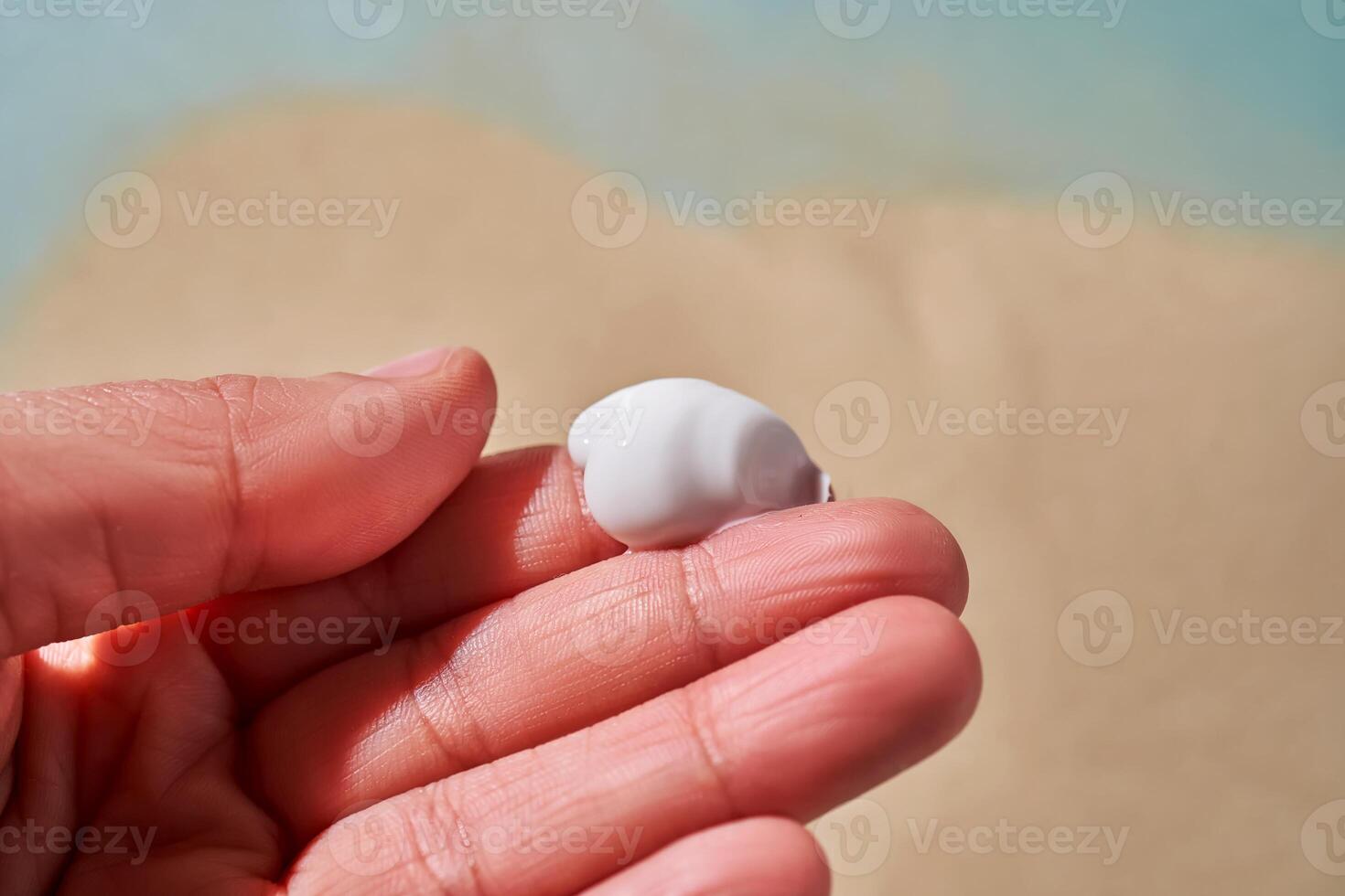 A smear of white cream with SPF on the fingers against a background of sand. photo
