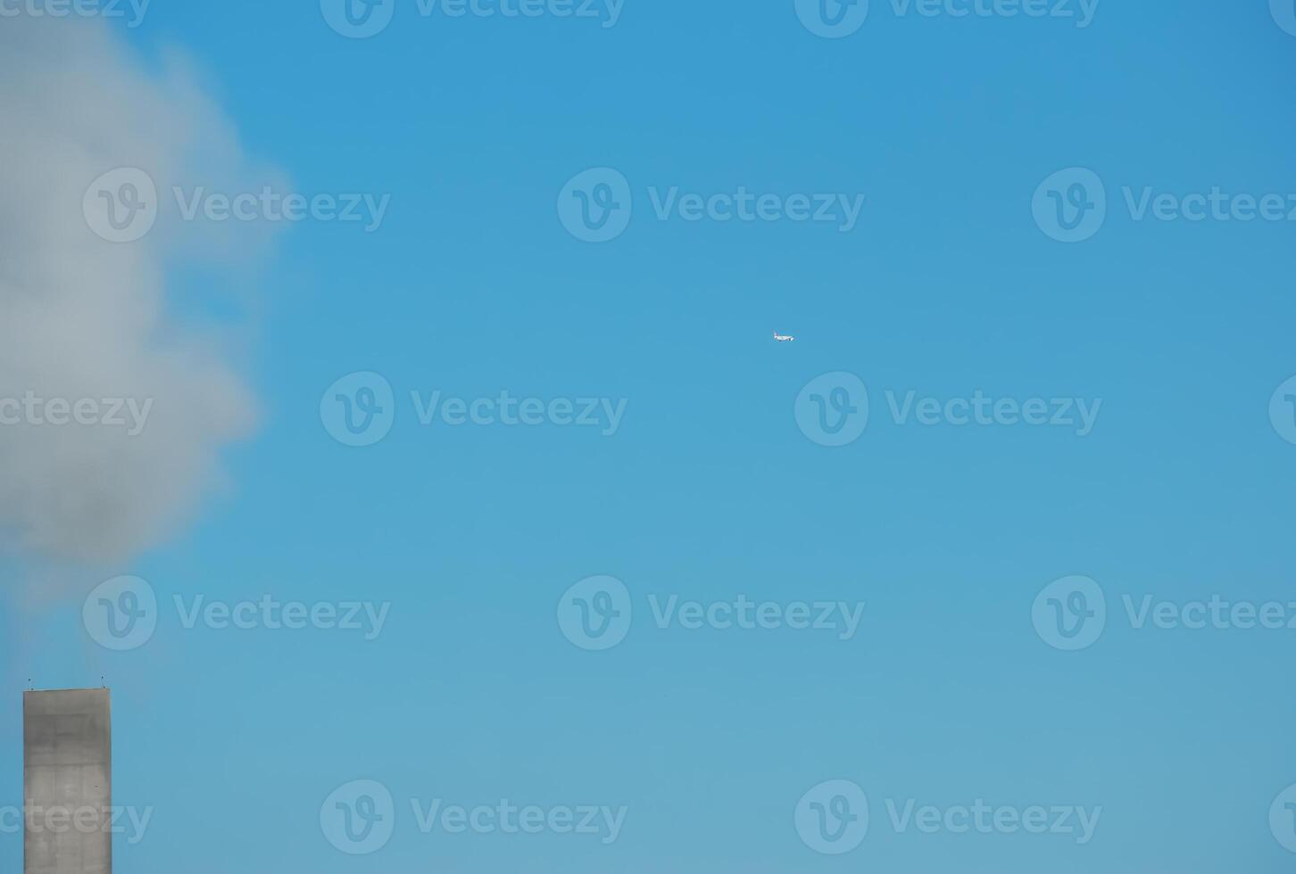 Smoke from a chimney and an airplane against a background of blue sky on a sunny day. photo