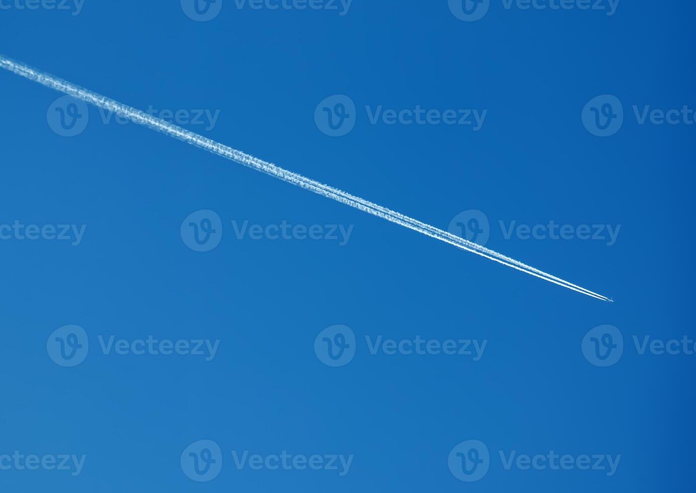 Airplane condensation trail and airplane on blue sky photo