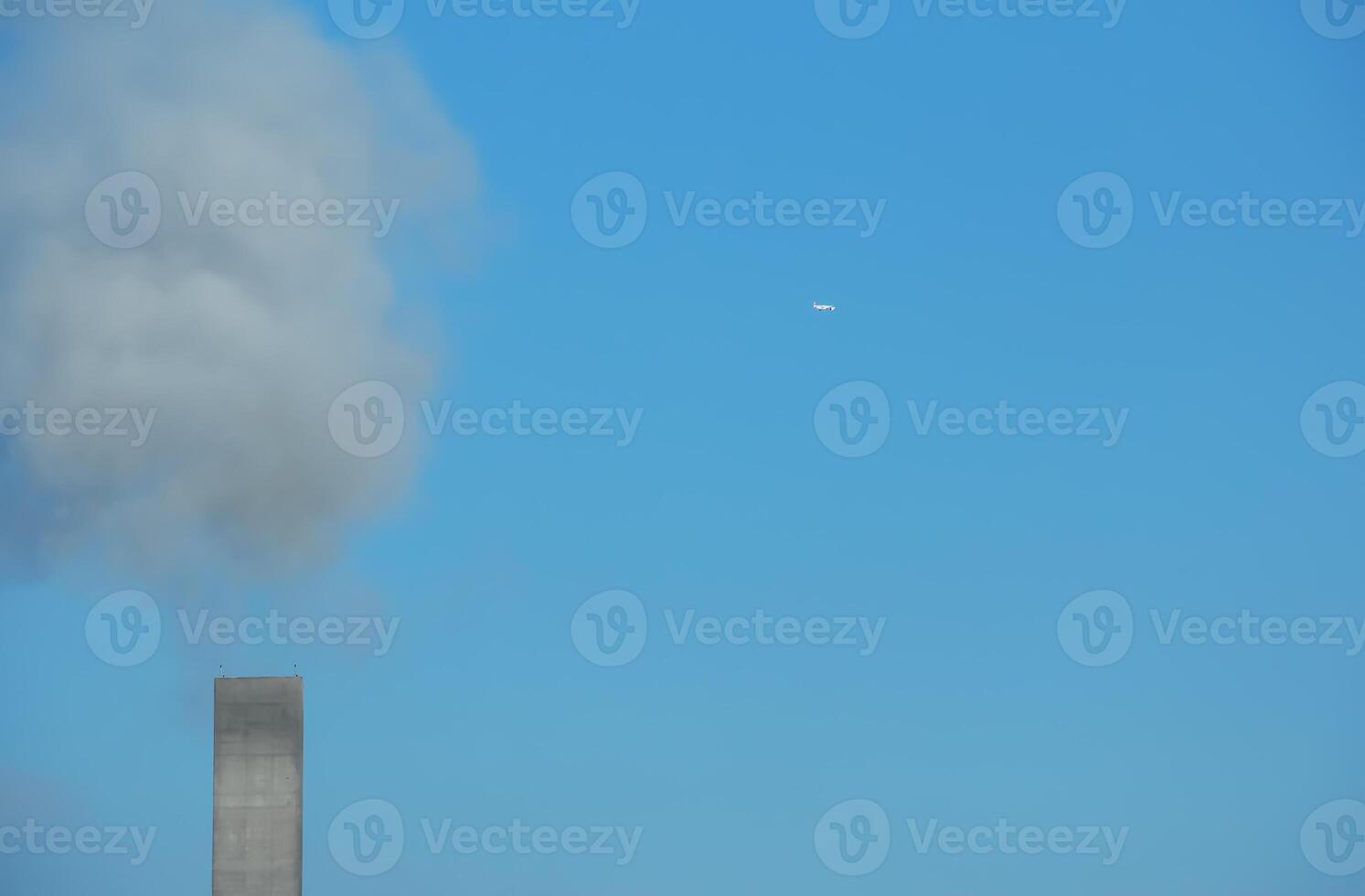 Smoke from a chimney and an airplane against a background of blue sky on a sunny day. photo